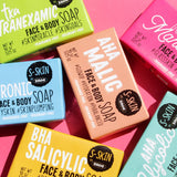 A variety of S-SKIN by Snoe AHA Mandelic Face and Body Soaps on a pink background.