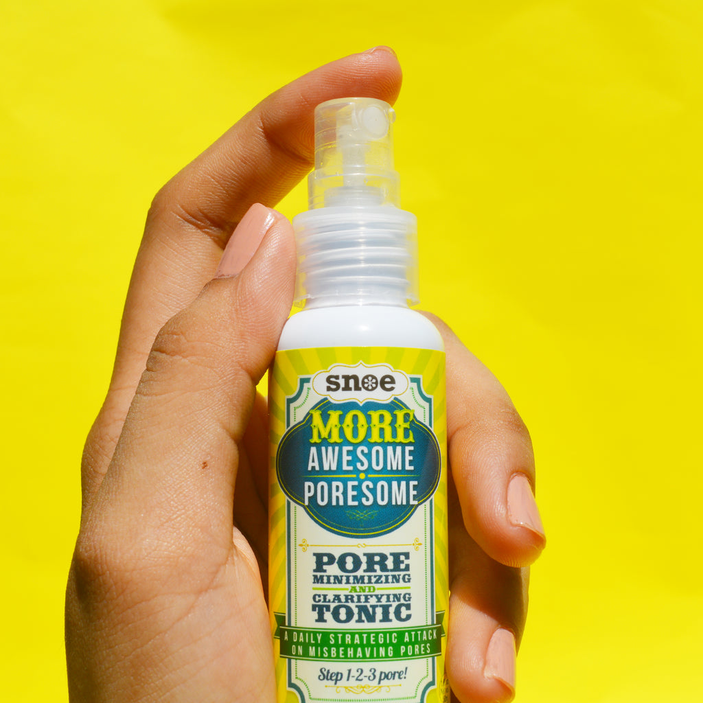 A person holding a bottle of More Awesome Poresome Cleanser, Toner & Serum Bundle Set | Pore Minimizing Pore Care Set by MORE AWESOME PORESOME on a yellow background.