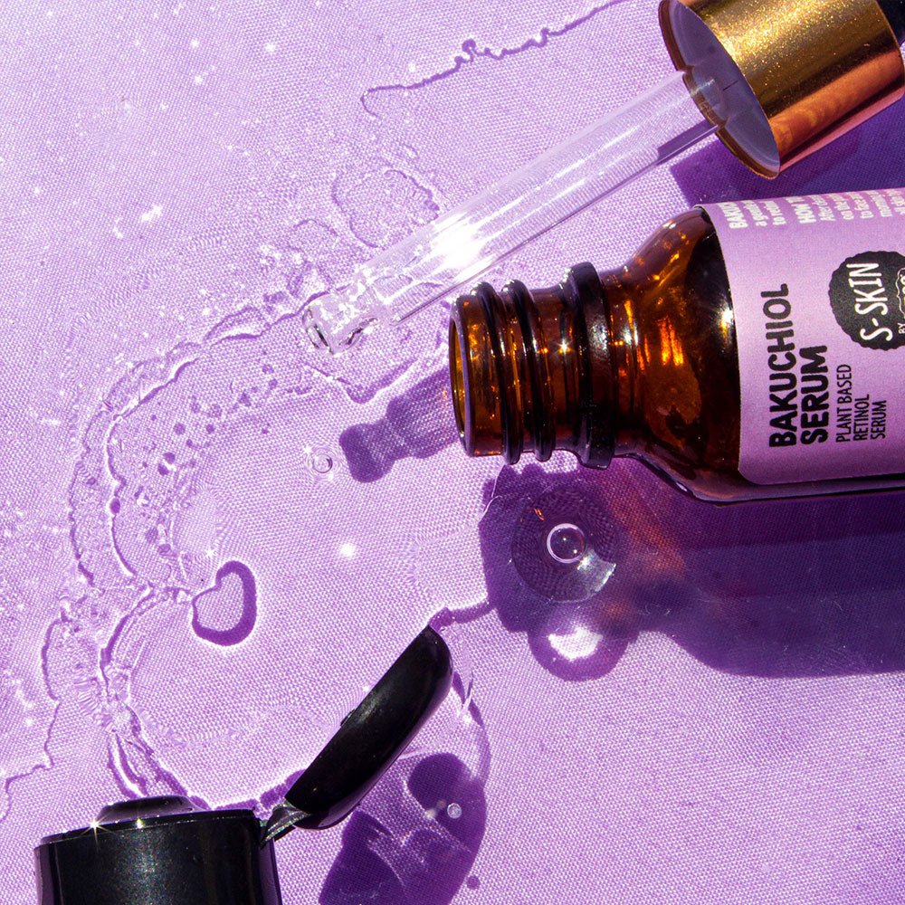 A bottle of Bakuchiol Facial Serum by S-SKIN, containing a plant-based alternative called Bakuchiol, placed alongside a bottle of water on a vibrant purple surface.