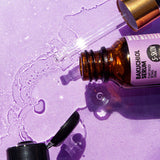 A bottle of Bakuchiol Facial Serum by S-SKIN, containing a plant-based alternative called Bakuchiol, placed alongside a bottle of water on a vibrant purple surface.