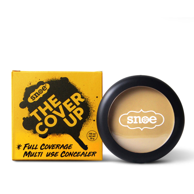 The yellow packaging of the "THE COVER UP" Buildable Concealer in PERFECT BEIGE, adorned with bold black text, epitomizes makeup excellence. Beside it, an open container with a black rim and transparent lid showcases this essential beige beauty product. The brand logo adorns both the box and lid, enhancing its allure.