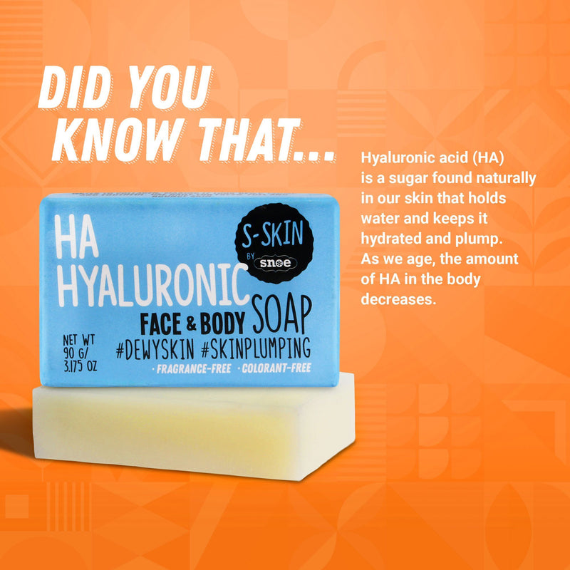 On an orange background adorned with geometric shapes rests a block of HA Hyaluronic Face and Body Soap by S-SKIN by Snoe. The packaging prominently displays “HA Hyaluronic” along with the hashtags “#dewyskin” and “#skinplumping.” To the left, text emphasizes hyaluronic acid's significant contribution to skin hydration, noting its natural decline with age and underscoring its importance in any beauty routine.