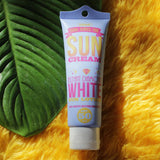 A tube of HERE COMES THE SUN CREAM's Instant Diamond White Sun Face & Body Lotion SPF 50++ sitting on top of a green leaf, emphasizing skincare.