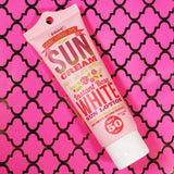 A tube of Instant Rosy White Sun Face & Body Lotion SPF 50++ from HERE COMES THE SUN CREAM on a pink background, providing skincare protection against harmful UV rays.