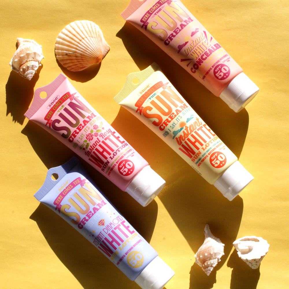Four tubes of HERE COMES THE SUN CREAM Instant Rosy White Sun Face & Body Lotion SPF 50++ and shells on a yellow background featuring beauty products.