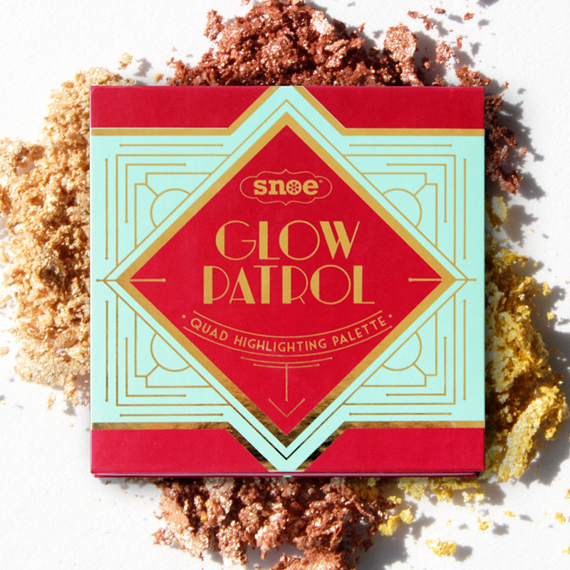 The image features the "Quad Highlighting Palette" from the beauty brand GLOW PATROL, with a geometric design on its cover. The makeup palette rests on a surface sprinkled with shimmering gold, bronze, and copper powders, accentuating the luxurious and radiant theme.