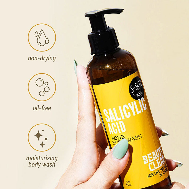 A close-up shows a person holding a brown bottle of "SALICYLIC ACID ACNE BODY WASH" by S-SKIN from Snoe, featuring a pump dispenser against a yellow background. Text on the left highlights its beauty benefits: non-drying, oil-free, and moisturizing. The bottle displays a yellow label with the phrase "BEAUTIFUL CLEAN.